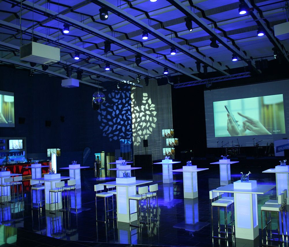 Der Saal 1 (Hauptsaal) des KOMSOS Der Saal 1 (Hauptsaal) des KOMSOS Berlin mit Hochtischbestuhlung und Ambientelicht.